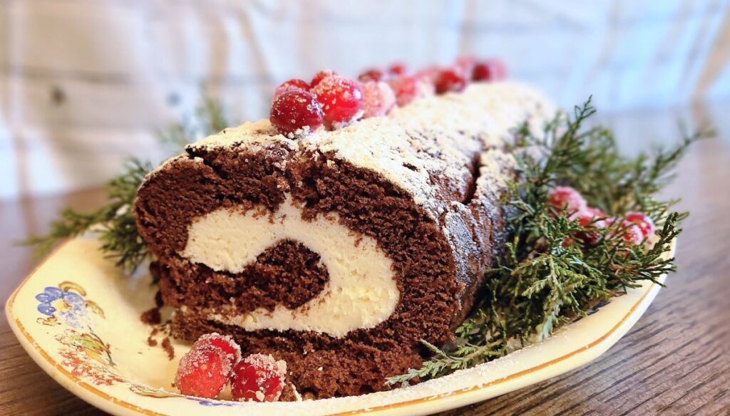 Yule log cake with powdered sugar and cranberries for the dessert portion of easy Yule dinner ideas and recipes for a magical feast. 