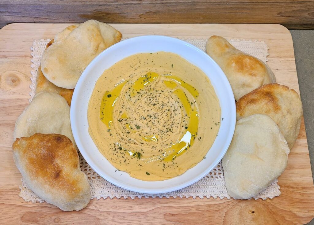 Easy high protein red lentil hummus with cashews in a while bowl with pita breads.