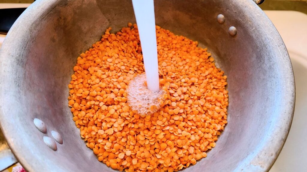 Rinsing red lentils in a metal colander. to make Easy high protein red lentil hummus with cashews.