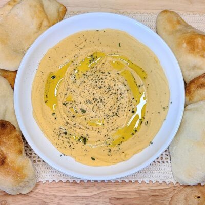Easy high protein red lentil hummus with cashews in a white bowl flanked with pita bread