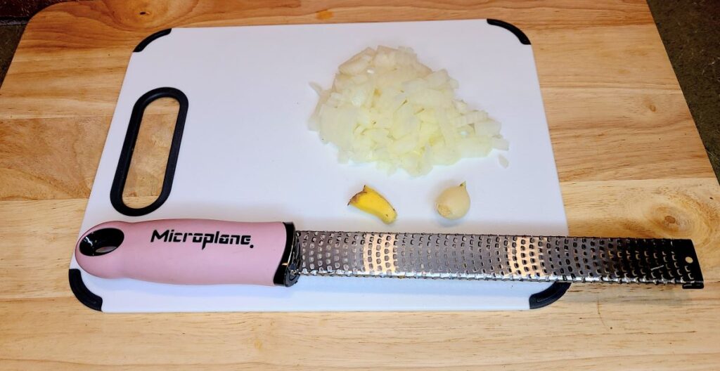Diced onion, piece of ginger and garlic on a cutting board with a rasp.