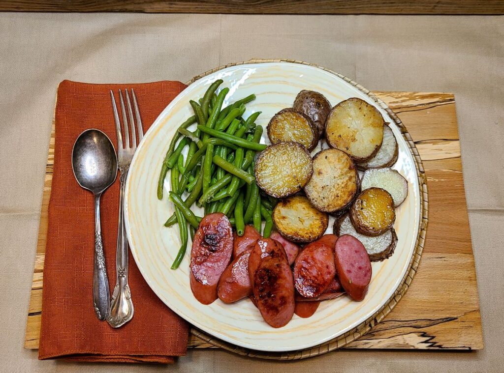  Easy Oven Roasted Potatoes With Rosemary Butter with green beans and smoked sausage on a plate with a fork and spoon