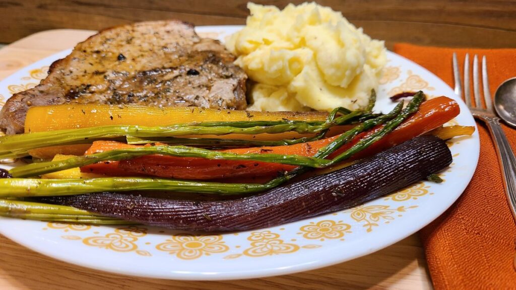 easy roasted carrots and asparagus recipe with maple glaze on a plate with a pork chop and mashed potatoes.