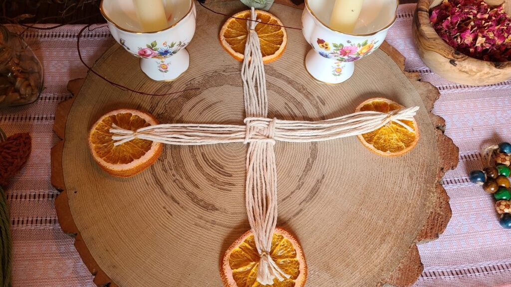 Imbolc altar with a white cotton St. Brigid cross, orange slices and candles. 