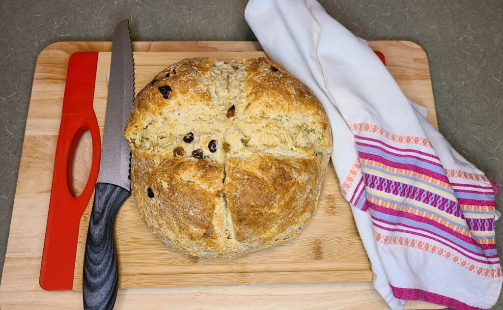  What the best cardamon Irish soda bread tastes like - round loaf on a wood board with a towel and a knife.