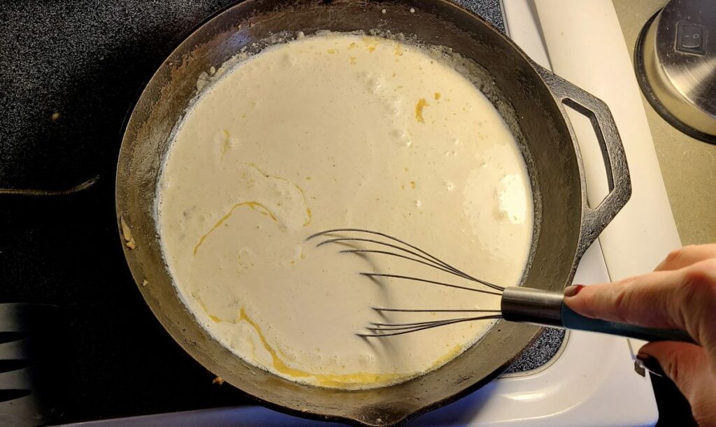 Whisking a bechamel sauce in a cast iron to make The ultimate make-ahead homemade green bean casserole.