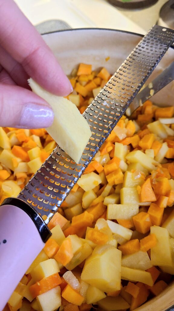 Hand grating ginger into a pot of Easy homemade farmhouse Irish vegetable soup with rosemary.