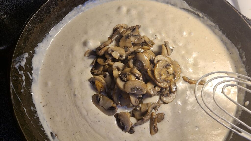 Adding mushrooms to a bechamel sauce in a cast iron pan. 