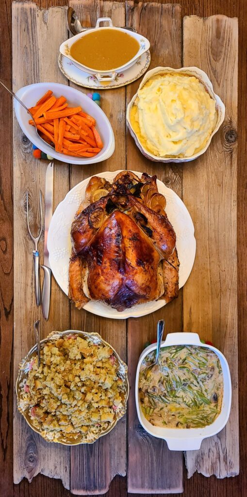 Beautiful arrangement of a terrific roasted French turkey with champagne and herbs and side dishes on a wooden board. Overhead view. 