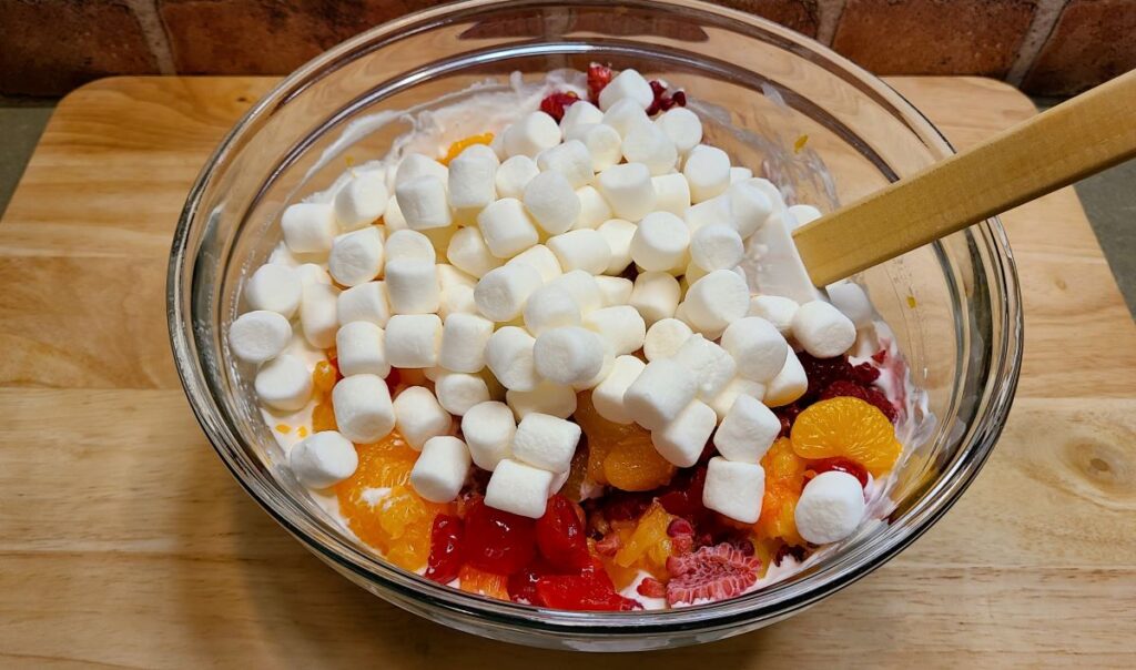 Mini marshmallows and fruit in a glass bowl for  how to make ambrosia fruit salad with whipped cream.