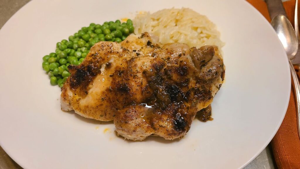 How To Perfectly Bake And Broil Boneless Chicken Thighs on a plate with peas and orzo.
